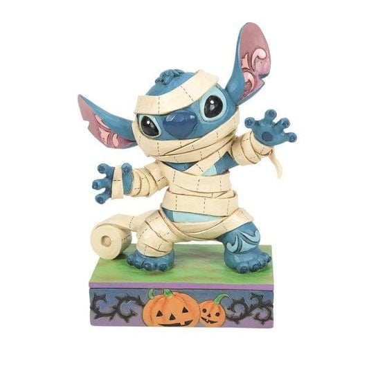 A blue alien character wrapped in mummy bandages stands on a decorated base with two carved pumpkins and a roll of bandages, evoking a Halloween theme. A blue alien character wrapped in mummy bandages stands on a decorated base with two carved pumpkins and a roll of bandages, evoking a Halloween theme.