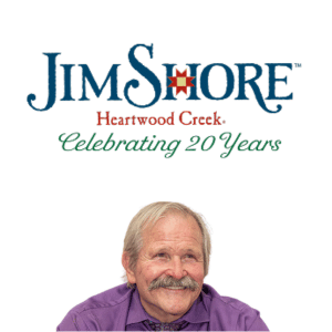 Logo for Jim Shore Heartwood Creek with the text Celebrating 20 Years above a smiling older man with a mustache, wearing a purple shirt, set against a white background.