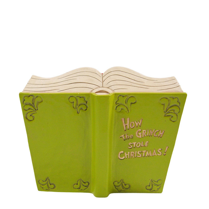 The Grinch By Jim Shore 6017056 is a ceramic storybook figurine featuring The Grinch with Cindy Lou & Max, a green cover titled How The Grinch Stole Christmas! in pink and yellow letters, ornate corners, and open pages on top.