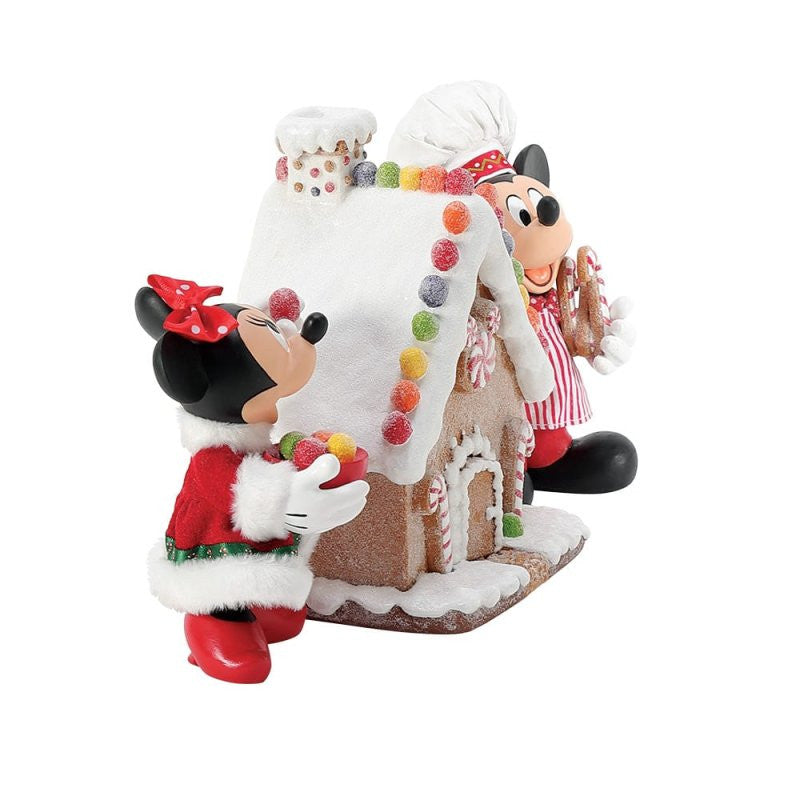 The Disney Mickey & Minnie’s Gingerbread House Possible Dreams Christmas Figurine by Department 56 (6016447) features Mickey & Minnie in festive outfits standing next to a candy-decorated gingerbread house, perfect for holiday décor.