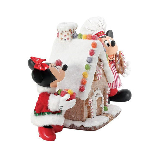 The Disney Mickey & Minnie’s Gingerbread House Possible Dreams Christmas Figurine by Department 56 (6016447) features Mickey & Minnie in festive outfits standing next to a candy-decorated gingerbread house, perfect for holiday décor.