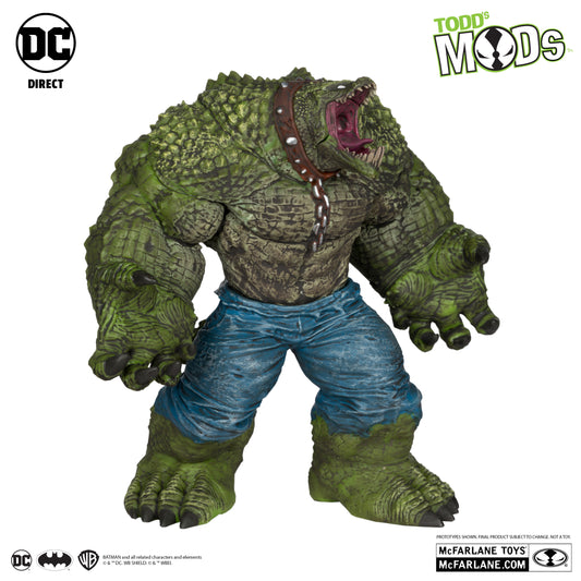 A bulky, green reptilian Killer Croc roars, showing sharp teeth and rough scales, wearing blue torn pants and a brown spiked collar. McFarlane Toys DC Direct Todds Mods edition gives off strong Suicide Squad vibes.