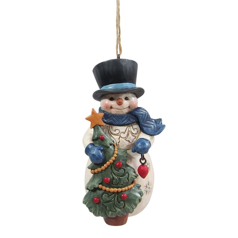 The Heartwood Creek By Jim Shore Snowman With Tree Hanging Ornament 6017301 features a snowman in a black top hat and blue scarf holding a festive Christmas tree, perfect for adding winter charm to your holiday décor.