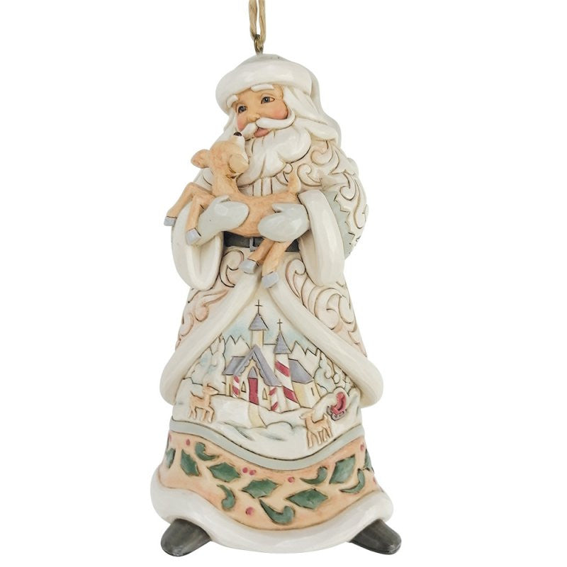 The Heartwood Creek By Jim Shore White Woodland Santa Holding A Fawn Hanging Ornament (6017181) features Santa in a cream robe with intricate patterns and a painted winter church scene at the base, holding a small fawn.