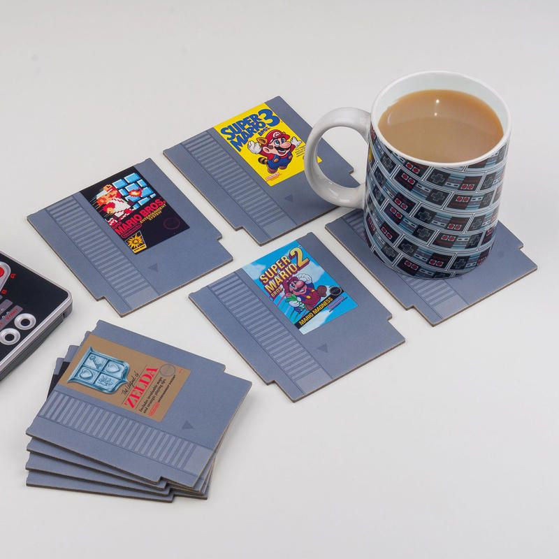 A mug of tea rests on a Paladone NES Cartridge Coaster, part of the NES Cartridge Coasters Set of 8 by Paladone, featuring retro gaming icons like Super Mario Bros. 2, Super Mario Bros. 3, and The Legend of Zelda.