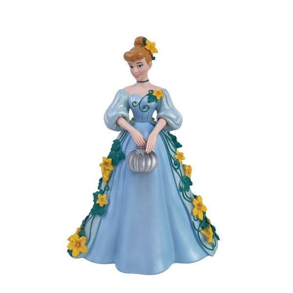 The Enesco Disney Showcase Cinderella Botanical Figurine 6015332 features Cinderella in a light blue gown with yellow flowers, green vines, a silver pumpkin, and updo brown hair adorned with a yellow flower.
