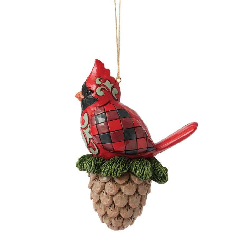 The Heartwood Creek By Jim Shore Cardinal On A Pinecone Hanging Ornament (6017030) features a festive cardinal on a pinecone with green swirls, perfect for adding holiday charm to your tree.
