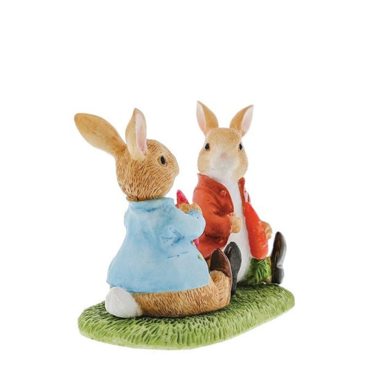 The Beatrix Potter Peter Rabbit & Benjamin Bunny Figurine by Beatrix Potter features two ceramic bunnies on green grass, one in a blue coat, the other in a red jacket, facing each other as if interacting, set against a white background.