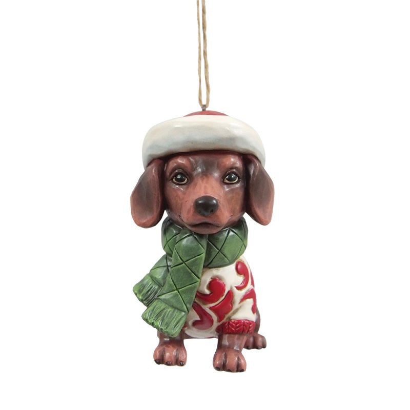 The Heartwood Creek By Jim Shore Christmas Dachshund Hanging Ornament (6017307) features a brown dachshund in a Santa hat, green scarf, and festive sweater—perfect whimsical holiday décor for your tree.