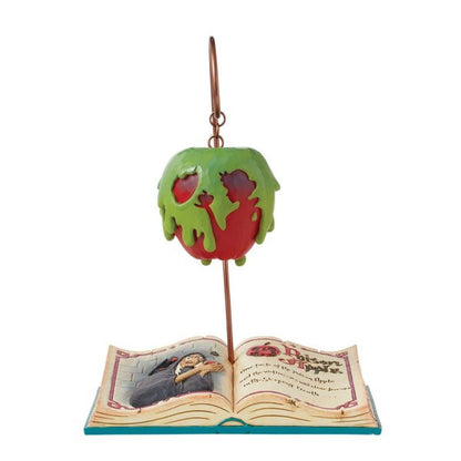 The Disney Traditions Apple-solutely Wicked (Poisoned Apple Book) by Jim Shore features a green poisoned apple with red base and dripping glaze, suspended above an open storybook of the Evil Queen from Snow White in signature Jim Shore style.