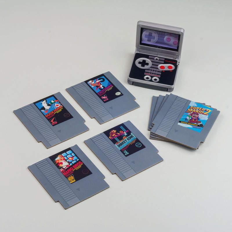 The NES Cartridge Coasters Set of 8 by Paladone features retro game-inspired designs, with each coaster resembling a classic NES cartridge and displayed near a handheld console-shaped case, perfect for fans of vintage gaming.