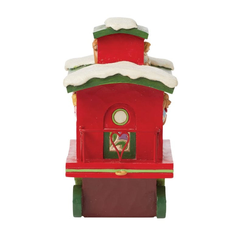 The Heartwood Creek By Jim Shore North Pole Delivery Train Car Caboose Figurine 6015481 features a red caboose with snow on the roof, green trim, and a heart-shaped metal detail on the back, as seen from the rear.