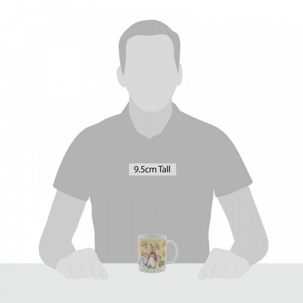 The Beatrix Potter Flopsy Bunny Mug, featuring a colorful design, is placed on a table in front of a person silhouette. The mug stands 9.5 cm tall.
