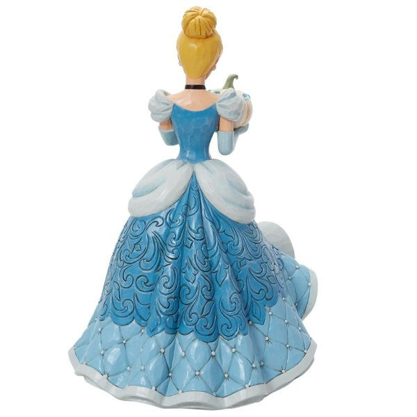 The Enesco Disney Traditions The Iconic Pumpkin Cinderella Deluxe Figurine by Jim Shore (6013078) shows Cinderella in a detailed blue and white gown, hair in a bun, holding a pumpkin, with intricate patterns on her dress.