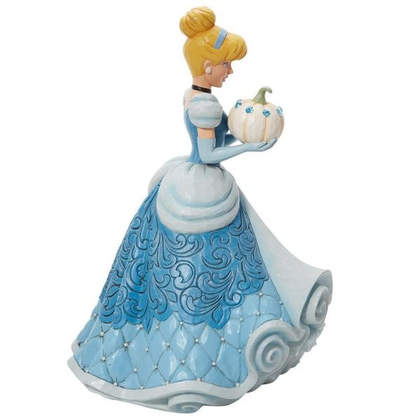 The Enesco Disney Traditions The Iconic Pumpkin Cinderella Deluxe Figurine by Jim Shore 6013078 features Cinderella in a blue gown holding a jeweled white pumpkin, with elegant patterns on her dress and scroll-like base.