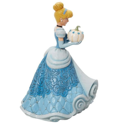 The Enesco Disney Traditions The Iconic Pumpkin Cinderella Deluxe Figurine by Jim Shore 6013078 features Cinderella in a blue gown holding a jeweled white pumpkin, with elegant patterns on her dress and scroll-like base.