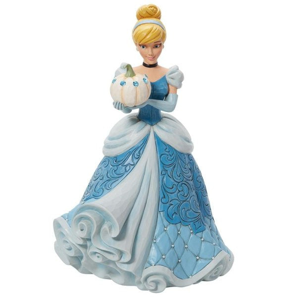 The Enesco Disney Traditions The Iconic Pumpkin Cinderella Deluxe Figurine by Jim Shore (6013078) shows Cinderella in a detailed blue ball gown, holding a white pumpkin, with her blonde hair in a bun and a gentle smile.