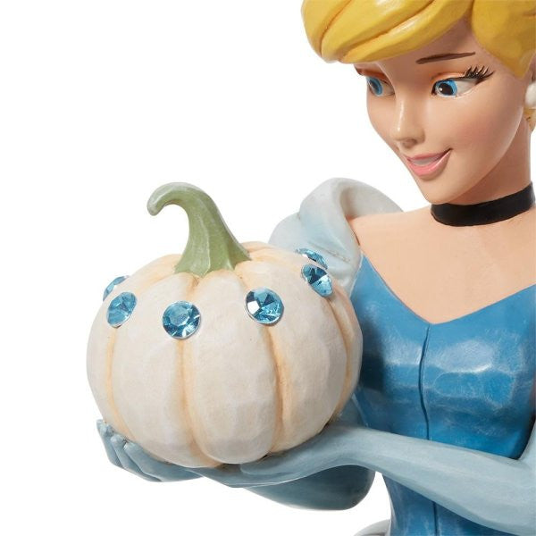 The Enesco Disney Traditions The Iconic Pumpkin Cinderella Deluxe Figurine by Jim Shore (6013078) shows Cinderellas upper body in a blue dress, smiling as she holds a jeweled white pumpkin—capturing a magical scene from the classic story.