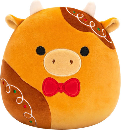 Squishmallows Jericho the Gingerbread Cow is a round, plush collectible featuring small white horns, black eyes, a beige snout, red bow tie, and gingerbread-inspired icing accents—perfect for fans of the Squishmallows brand.
