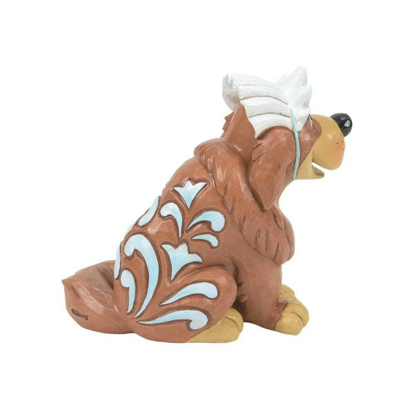 The Disney Traditions Nana Mini Figurine 6014333 features a brown dog with blue and white patterns, happily sitting to the right and wearing a white feathered headdress.