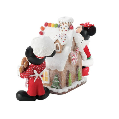 The Department 56 Disney Mickey & Minnie’s Gingerbread House Possible Dreams Figurine (6016447) features Mickey and Minnie in festive outfits by a candy-decorated gingerbread house, with Mickey holding cookies and Minnie peeking around the side.