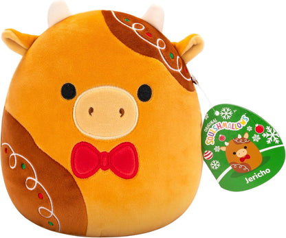 Squishmallows Jericho the Gingerbread Cow is a round collectible plush styled like gingerbread with icing details and a red bow tie, complete with a Squishmallows tag.