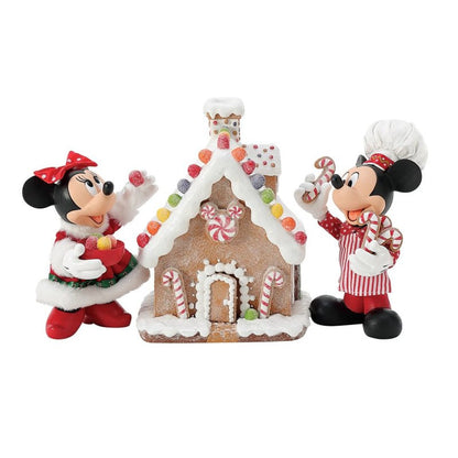 The Disney Mickey & Minnie’s Gingerbread House Possible Dreams Christmas Figurine by Department 56 (6016447) features Mickey and Minnie in festive outfits with candy, standing next to a sweetly decorated gingerbread house.
