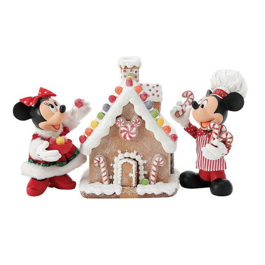 The Disney Mickey & Minnie’s Gingerbread House Possible Dreams Christmas Figurine by Department 56 (6016447) features Mickey and Minnie in festive outfits with candy, standing next to a sweetly decorated gingerbread house.
