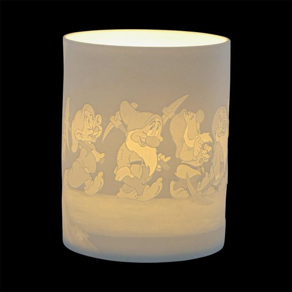 The Disney Enchanting Collection Diamond Shine (The Seven Dwarfs) Ceramic Lithophane Lamp A31088 features engraved images of the Seven Dwarfs marching around its white cylindrical surface, glowing warmly against a solid black background.