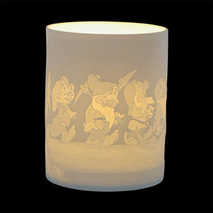 The Disney Enchanting Collection Diamond Shine (The Seven Dwarfs) Ceramic Lithophane Lamp A31088 features engraved images of the Seven Dwarfs marching around its white cylindrical surface, glowing warmly against a solid black background.