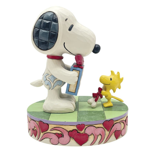The Snoopy Valentines Figurine by Peanuts By Jim Shore features Snoopy with a blue gift box facing Woodstock holding a bone with a red bow, both on a heart and swirl base—an ideal Valentine’s Day décor piece.