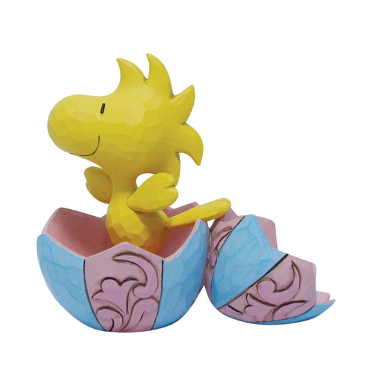 The Woodstock Popping out of an Egg Mini Figurine by Peanuts By Jim Shore features Woodstock cheerfully smiling and looking up as he emerges from a pastel blue and pink cracked egg, perfect for a charming Easter display.