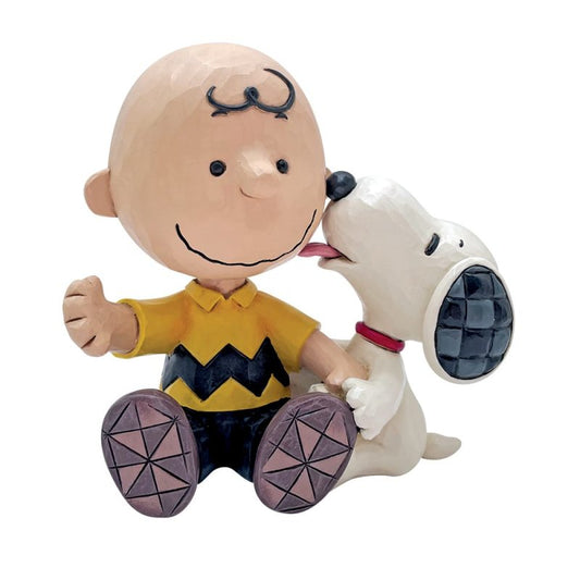 The Charlie Brown with Snoopy Figurine by Peanuts By Jim Shore shows Charlie in his yellow zigzag shirt as Snoopy, with a red collar, licks his cheek. This charming piece captures their joyful friendship in classic Jim Shore style.