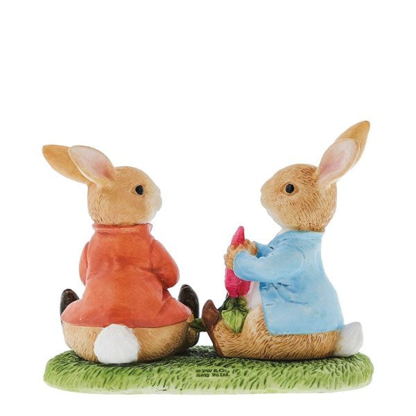 The Beatrix Potter Peter Rabbit & Benjamin Bunny Figurine features two ceramic bunnies on grass, one in a red coat, the other in blue holding a pink flower. Both have white tails and large ears. Brand: Beatrix Potter.