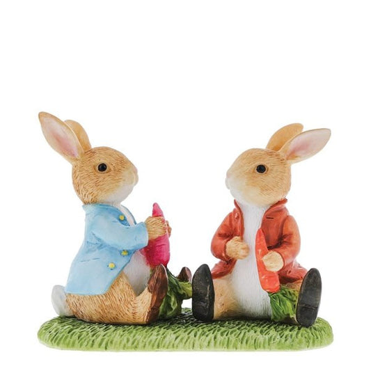 The Beatrix Potter Peter Rabbit & Benjamin Bunny Figurine by Beatrix Potter features two smiling bunnies in blue and red coats, each with a red carrot, sitting on green grass and facing each other—evoking the charm of classic tales.