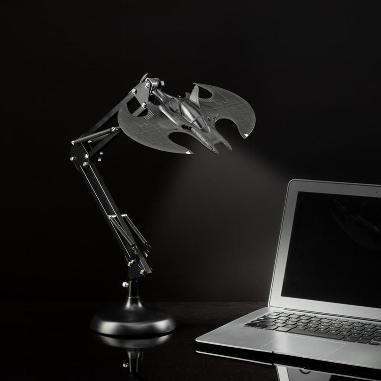 The Batman Batwing Posable Desk Light V2 by Paladone shines onto an open laptop with its adjustable arm, making it a perfect Batman-themed home accessory and stylish desk light from Paladone.