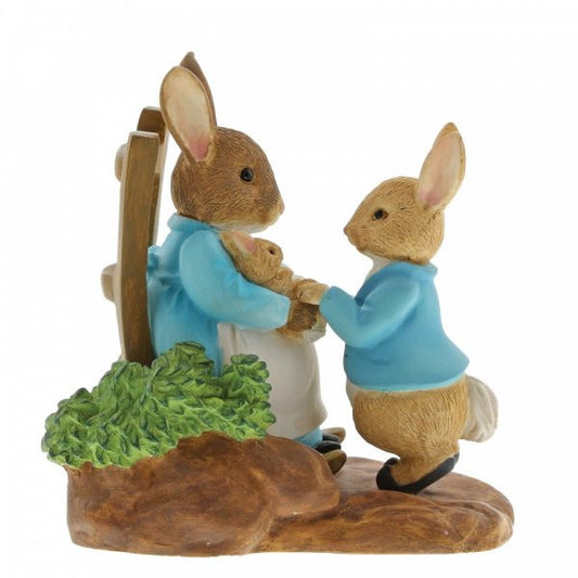 The Beatrix Potter At Home by the Fire with Mummy Rabbit Figurine features three affectionate rabbits in blue jackets, holding hands on a grassy base—a charming collectible gift from the Beatrix Potter brand.