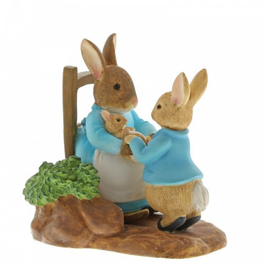 The Beatrix Potter At Home by the Fire with Mummy Rabbit figurine features three rabbits in blue jackets on a brown base with green foliage—a collectible gift by Beatrix Potter perfect for fans and collectors.