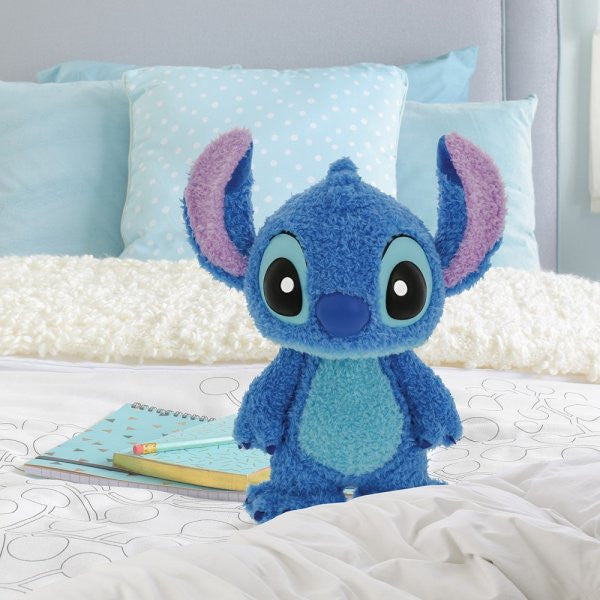 The Grand Jester Studios Disney Grand Jester Studios Fluffy Stitch Figurine 6015952, with poseable arms and head, sits on a bed with white and blue bedding—a perfect Disney fan gift. A notebook, pencil, pillows, and light headboard complete the cozy scene.