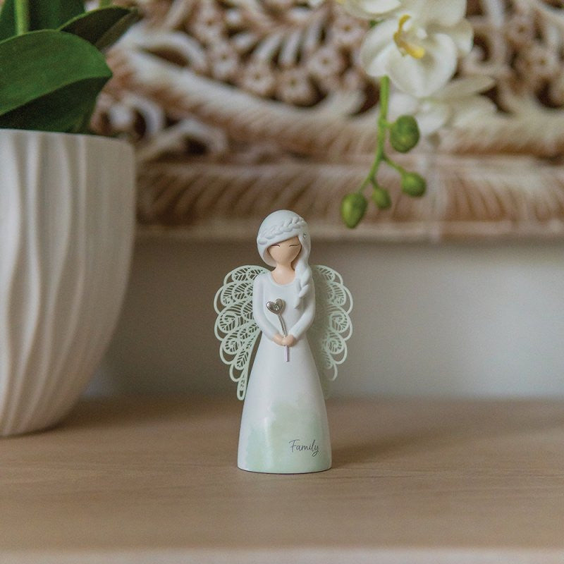 The You Are An Angel Family Angel Figurine ASF021 features delicate wings and a white dress inscribed with “Family,” standing beside a potted plant and orchids—perfect as home decor or a thoughtful gift.