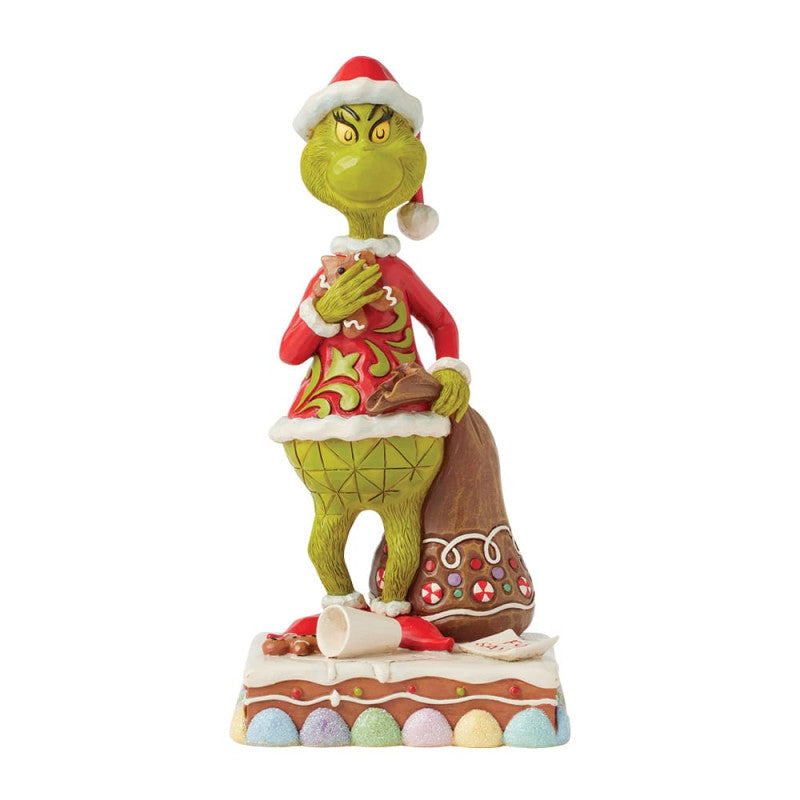 The Grinch Eating Cookies Figurine by Jim Shore (6017058) features The Grinch in a red Santa hat and coat, holding a brown sack with candy patterns, standing on a festive base. From The Grinch By Jim Shore collection.