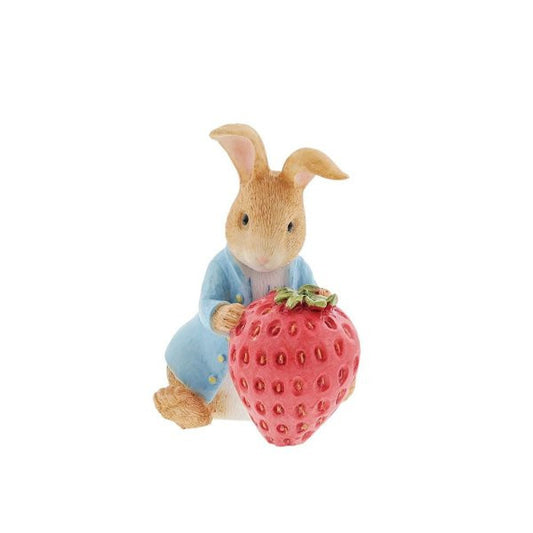 The Beatrix Potter Peter Rabbit with Strawberry Figurine features the beloved character in a blue jacket holding a red strawberry, inspired by Beatrix Potter, set against a plain white background.