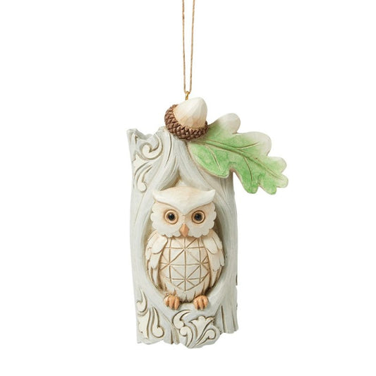 The Heartwood Creek By Jim Shore White Woodland Owl In Tree Hanging Ornament (6017182) features a carved owl with a geometric chest, perched in a tree hollow with leaf and acorn accents, capturing woodland charm.