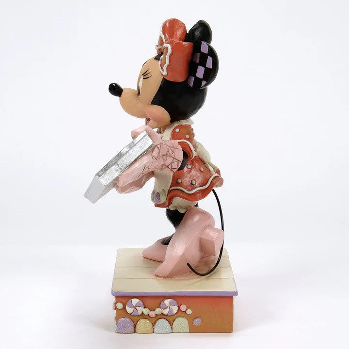 The Disney Traditions Pre-Order Baking Bliss (Minnie Gingerbread Cookies) Figurine by Jim Shore (6016881) features Minnie Mouse kneeling on a pastel platform, holding a silver tray, in signature whimsical style.