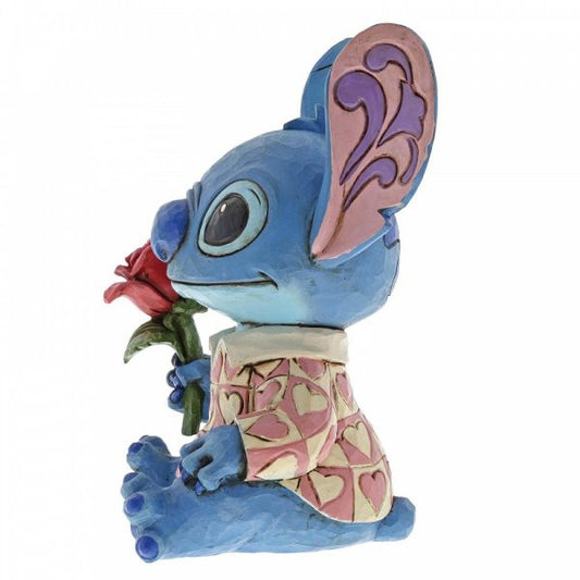 Disney Traditions Stitch the adorable alien from Lilo & Stitch wears a heart-patterned shirt as he offers a single red rose figurine
