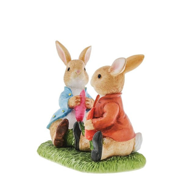 The Beatrix Potter Peter Rabbit & Benjamin Bunny Figurine features two ceramic rabbits in blue and red jackets, seated on green grass with carrots, cheerfully facing each other. Brand: Beatrix Potter.