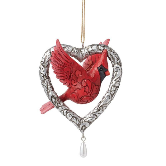 The Heartwood Creek By Jim Shore Forever In My Heart (Caring Cardinal) Hanging Ornament features a detailed red cardinal inside a silver heart-shaped frame with intricate designs and a dangling white teardrop bead.
