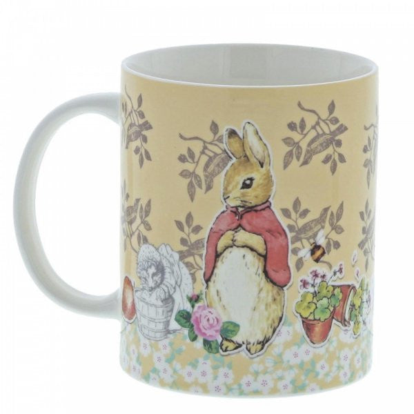 The Beatrix Potter Flopsy Bunny Mug features a rabbit in a red cape with flowers, a basket, and potted plants on a light yellow floral-patterned background—a charming tribute to the beloved classic.