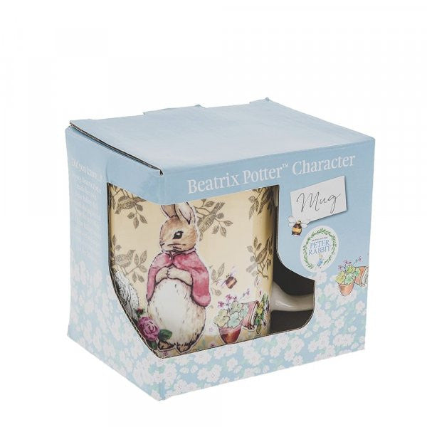 A ceramic Flopsy Bunny Mug by Beatrix Potter with a rabbit illustration peeks from a light blue, floral-patterned box labeled Beatrix Potter Character Mug.