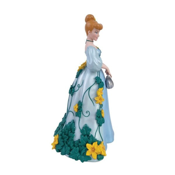 The Enesco Disney Showcase Cinderella Botanical Figurine 6015332 features Cinderella in a blue gown adorned with green vines and yellow flowers, silver clutch in hand, hair in a bun, from the Botanical Collection.